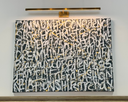 Abstract artwork with text on a white wall, illuminated by a light fixture.
